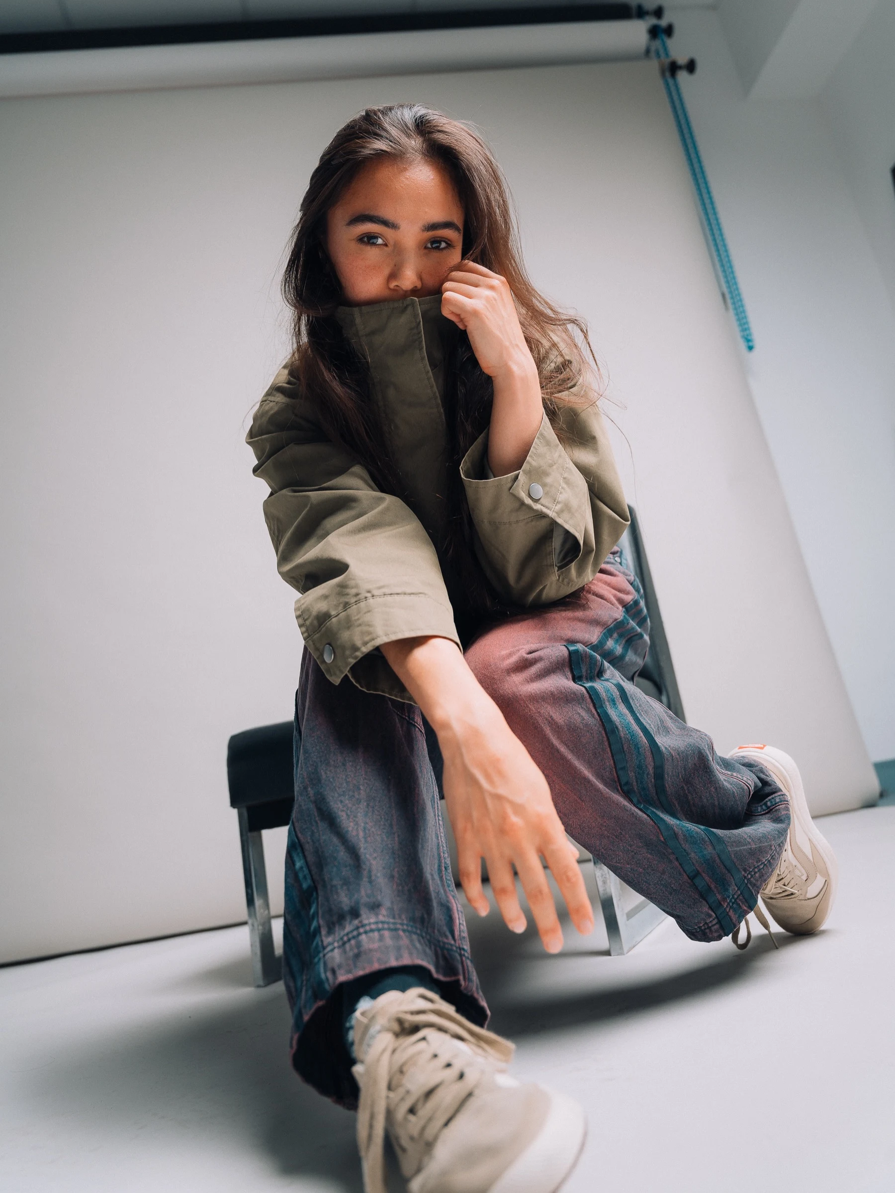 Baggy two-tone striped jeans paired with an oversized olive jacket and beige sneakers.