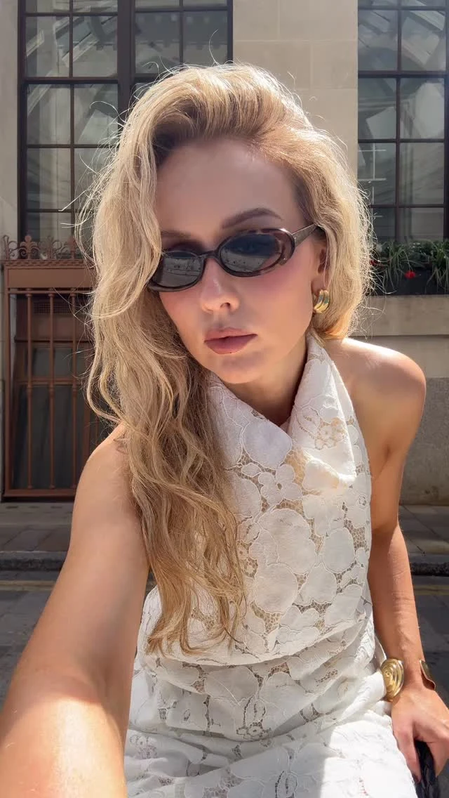 The outfit is a white sleeveless dress with a high halter-style neckline and an all-over large floral lace pattern. The fitted bodice has a draped, folded section across the front, and the skirt is visible at the bottom of the image.