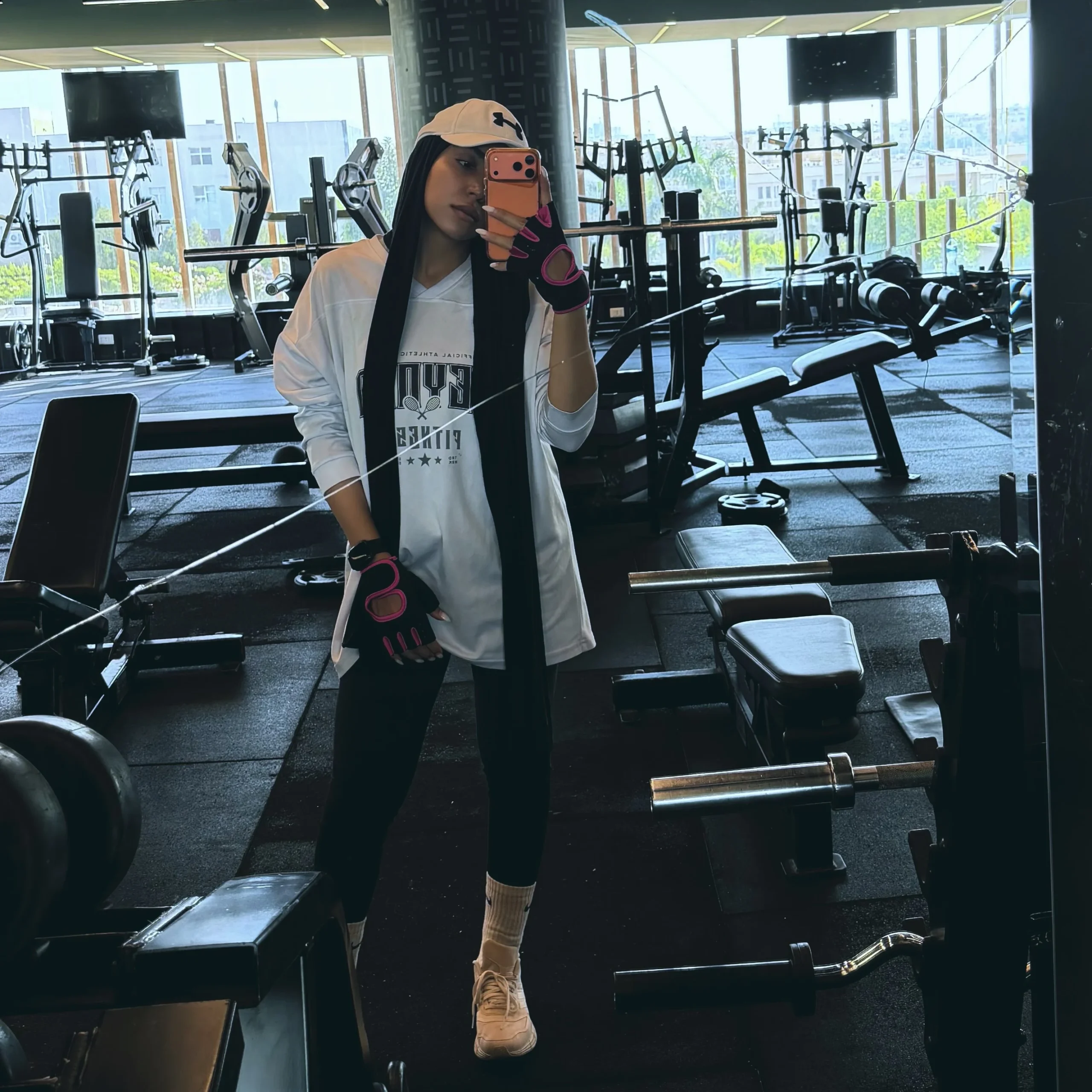 White graphic hoodie, black leggings, peach cap and sneakers with pink-accented fingerless gloves.