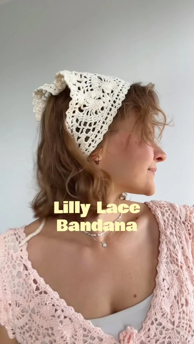 Person wearing a cream lace headscarf and pale pink openwork cardigan with a pendant necklace.