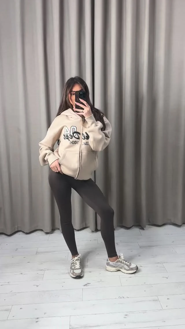 beige zip-up hoodie with black graphic print, black leggings, white chunky sneakers