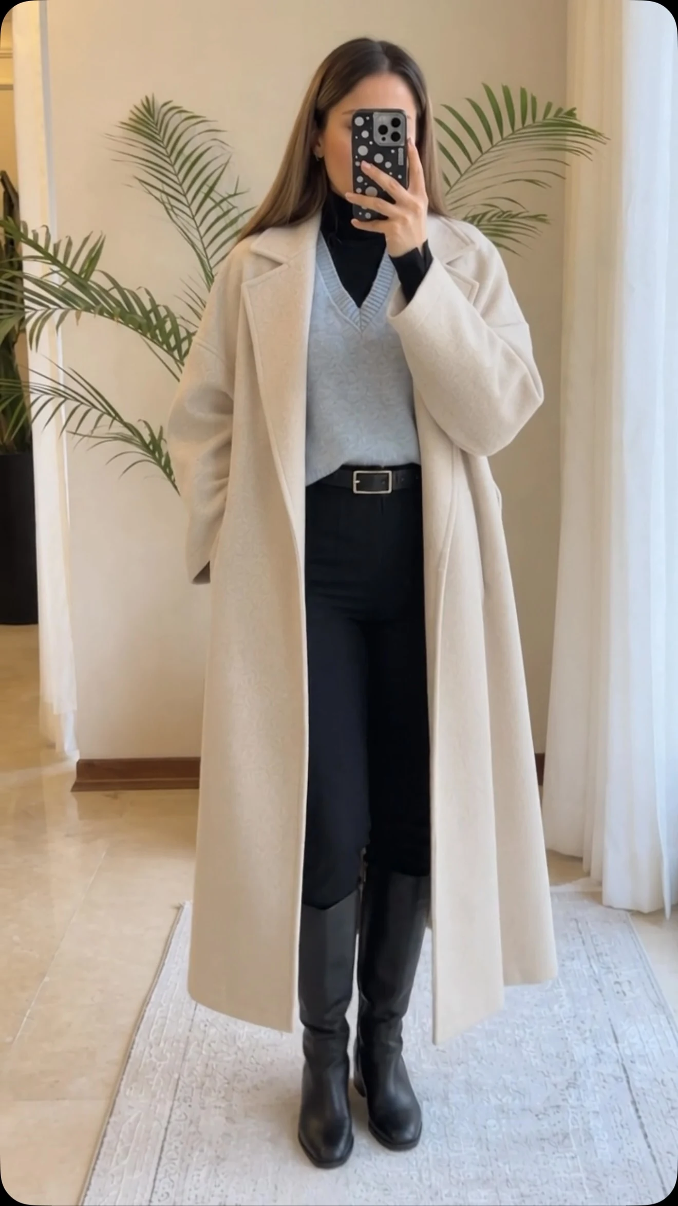 Open black coat over grey sweater vest, black turtleneck, trousers, and knee-high boots.