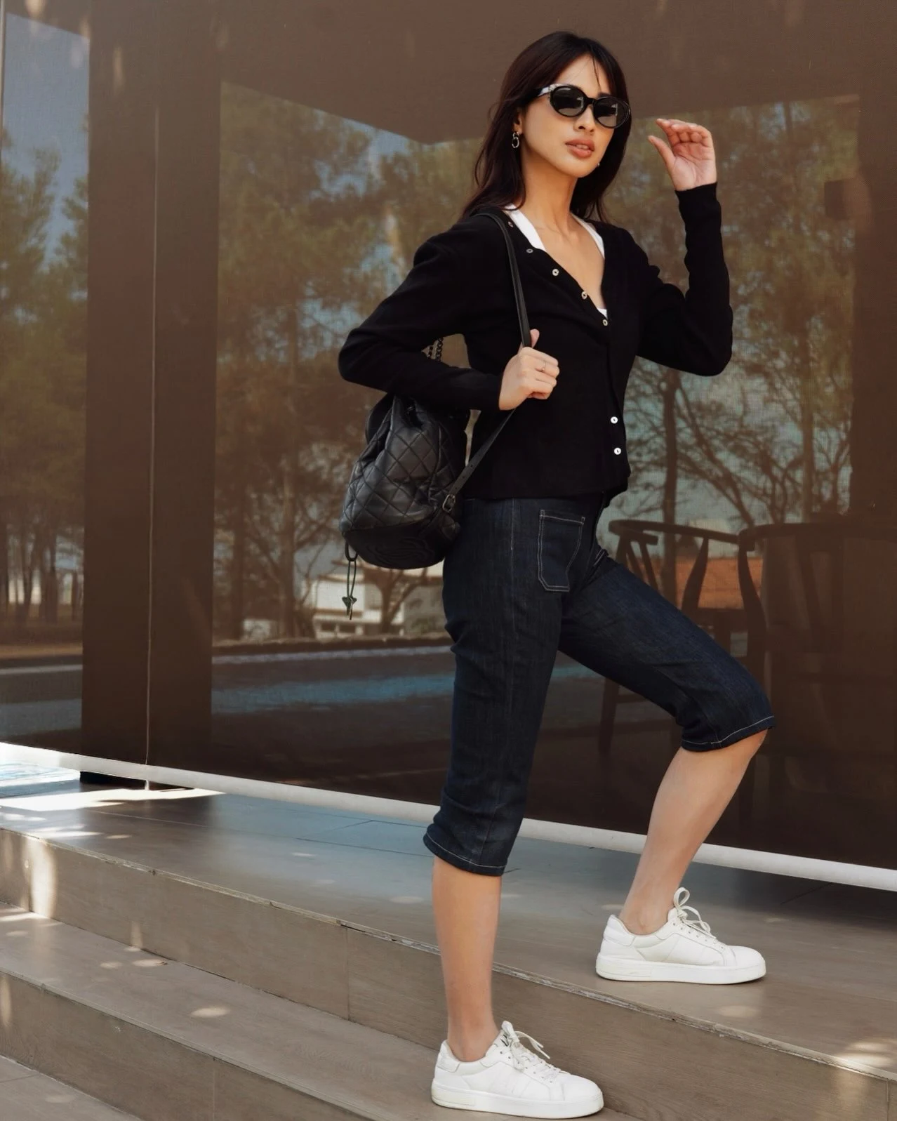 Black knit cardigan worn open over a white top and blue straight jeans.