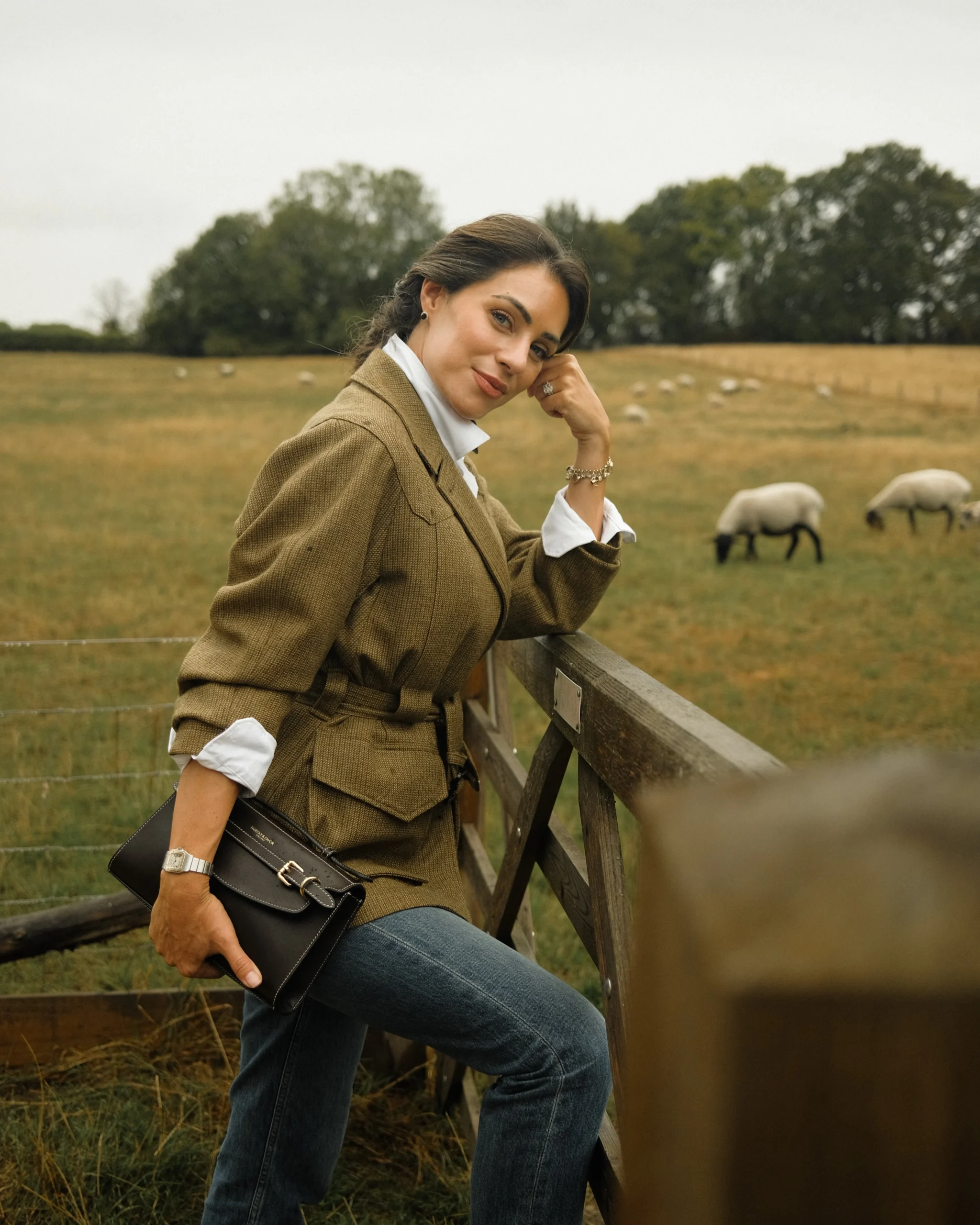 Brown tweed belted jacket, white collared shirt, blue jeans, brown tall riding boots, patterned neck scarf