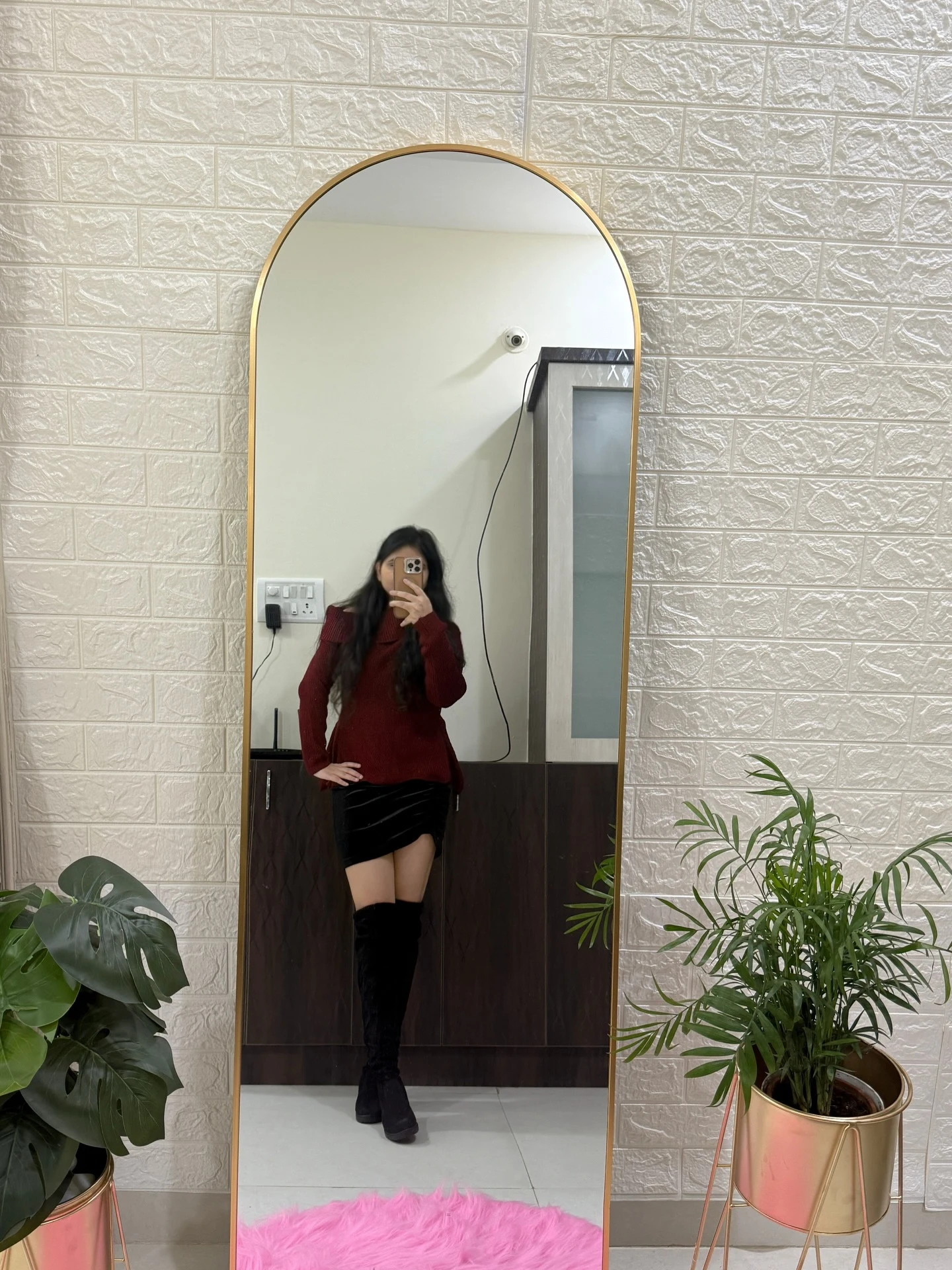 Woman in a burgundy off-shoulder knit sweater, black velvet mini skirt, and over-the-knee boots.