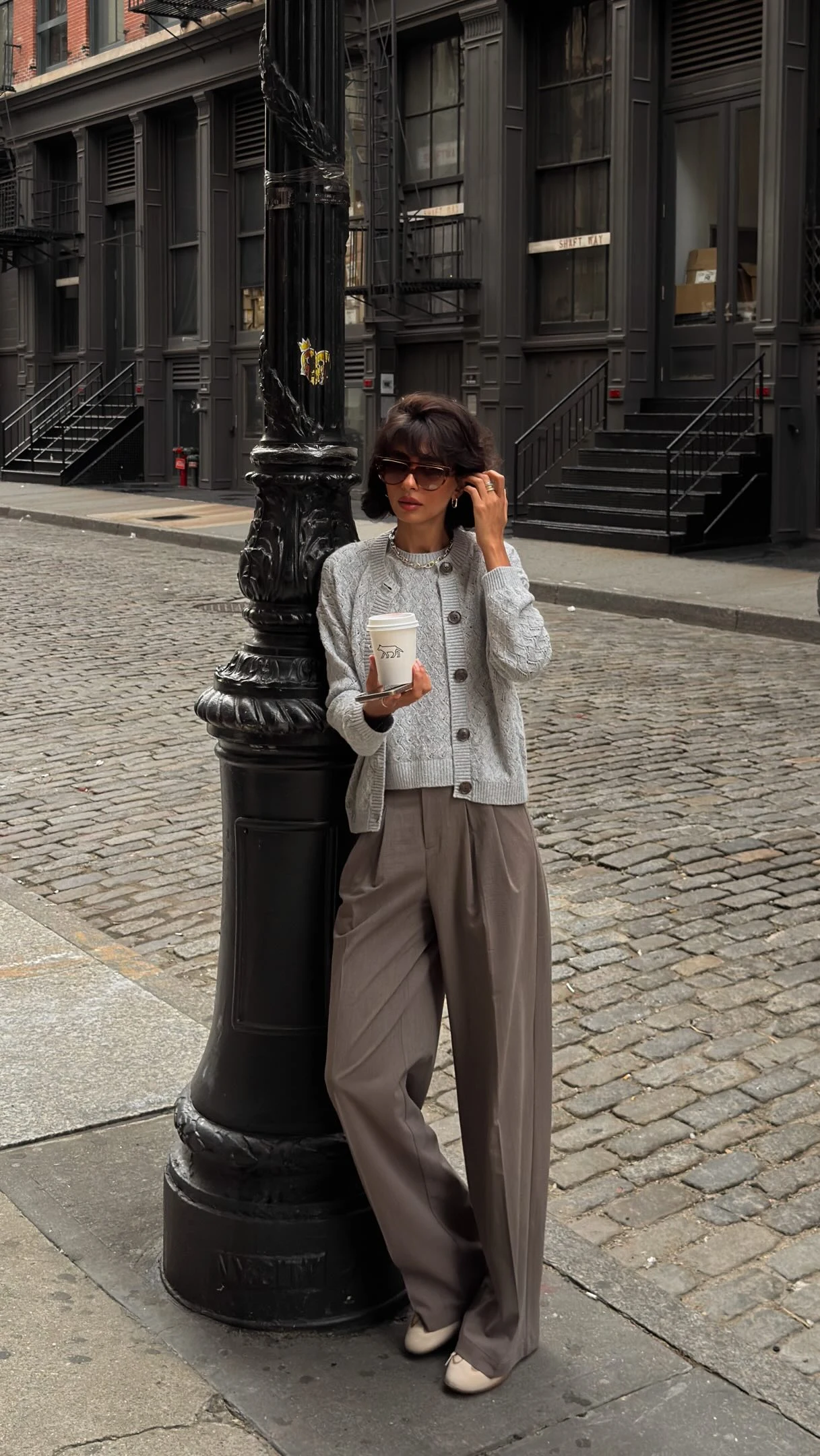 Beige sleeveless cable-knit V-neck sweater vest, white top, tailored white shorts, white sneakers