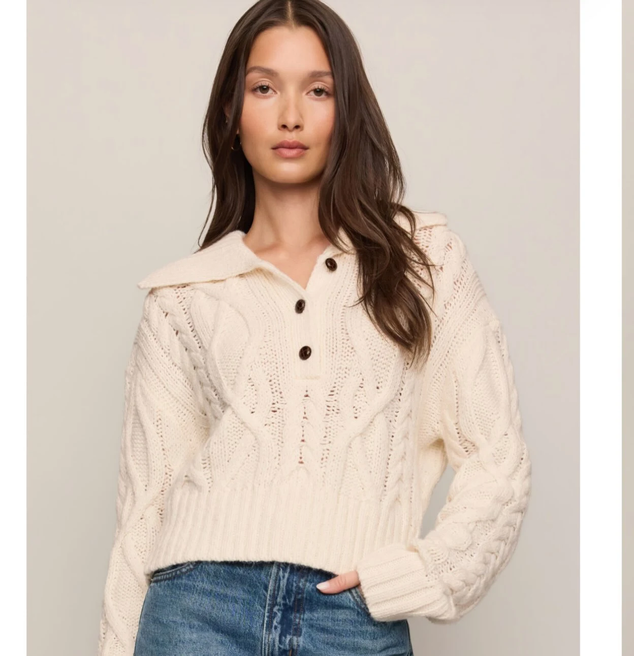Cream cropped cable-knit sweater with collar and dark buttons worn over blue denim jeans.