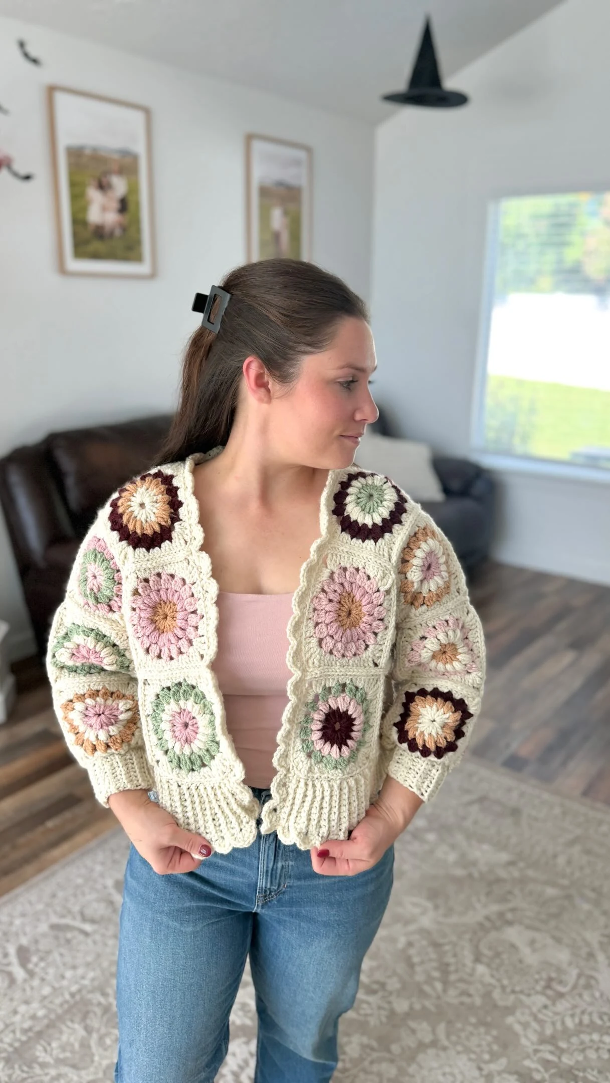 Cream granny square cardigan with floral motifs over a pale pink top and blue jeans.