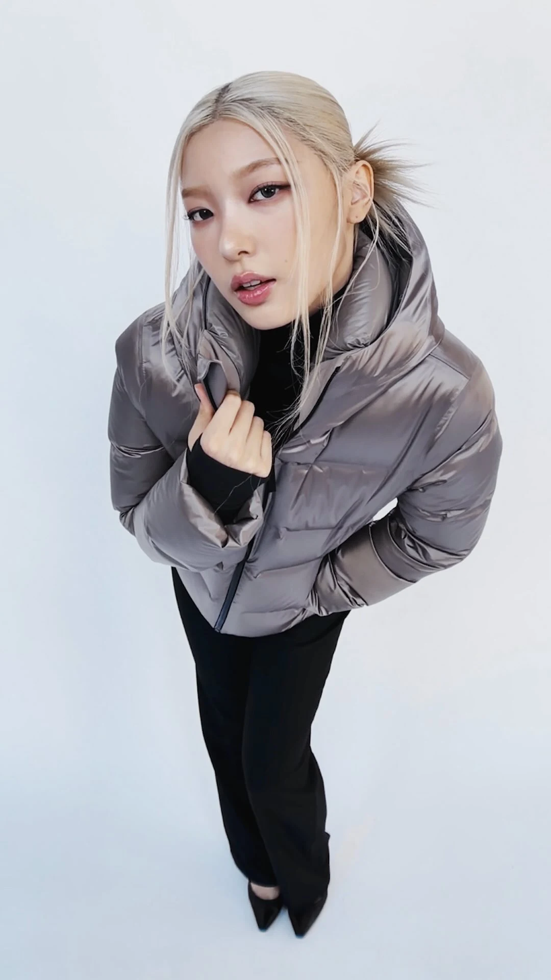 Shiny gray boxy cropped puffer jacket worn over a black top and black straight-leg pants.