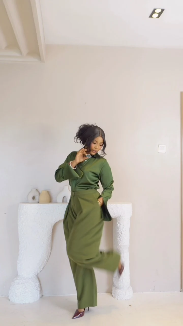 Olive-green wrap top and matching pleated wide-leg trousers styled with dark pointed shoes and a small handbag.