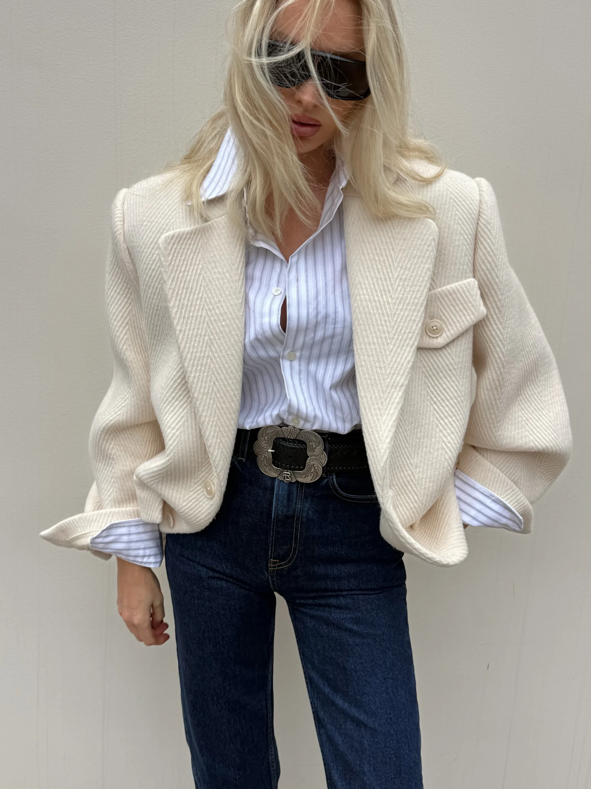 Oversized ivory herringbone blazer worn over a striped shirt tucked into dark indigo jeans with a black belt.