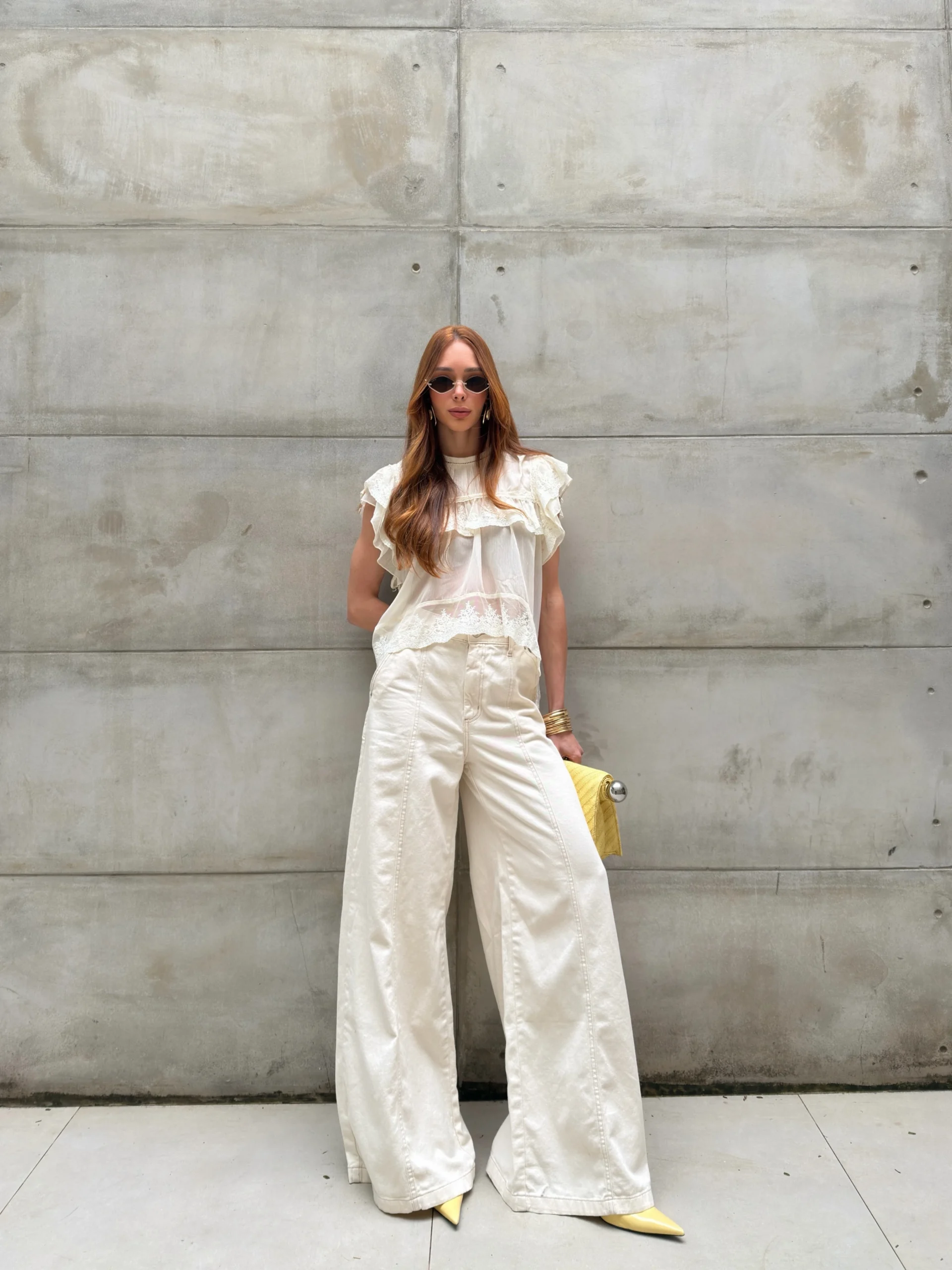 Sheer ivory ruffled blouse and wide ivory trousers styled with yellow pointed-toe shoes and gold bangles.