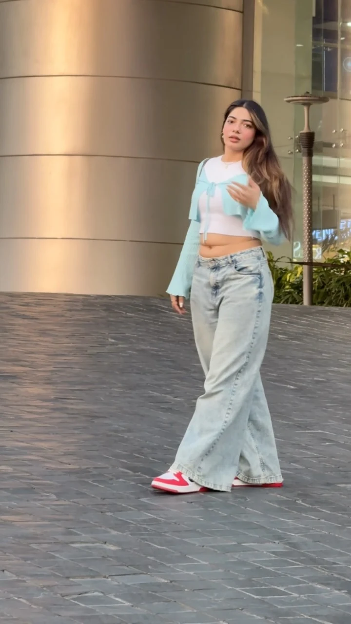 Light-wash baggy jeans with a tied blue cropped cardigan, white crop top, and red sneakers.