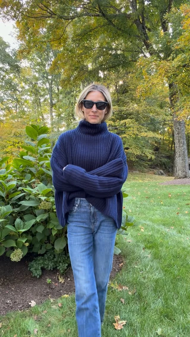 Person in navy ribbed turtleneck and high-waist light blue jeans with dark sunglasses.