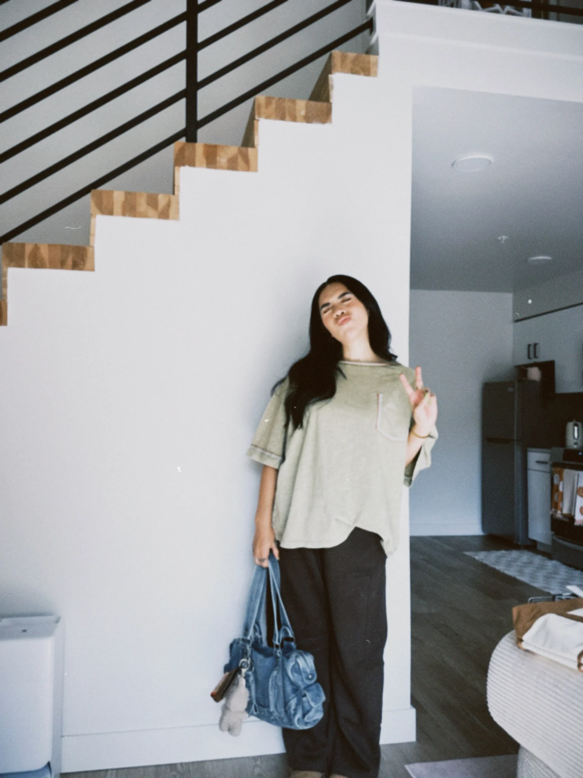 Olive green oversized tee with embroidered trim, dark wide-leg sweatpants, tan shoes, and a blue denim bag.