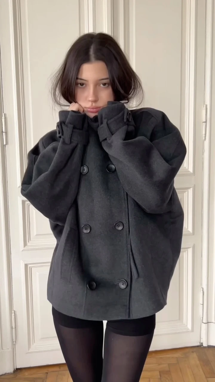 Dark charcoal oversized double-breasted wool coat, black top, black shorts, sheer black tights, knee-high black boots