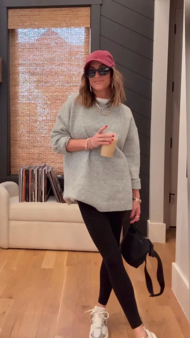 Light gray oversized dropped-shoulder sweater worn with fitted black leggings and white athletic shoes.