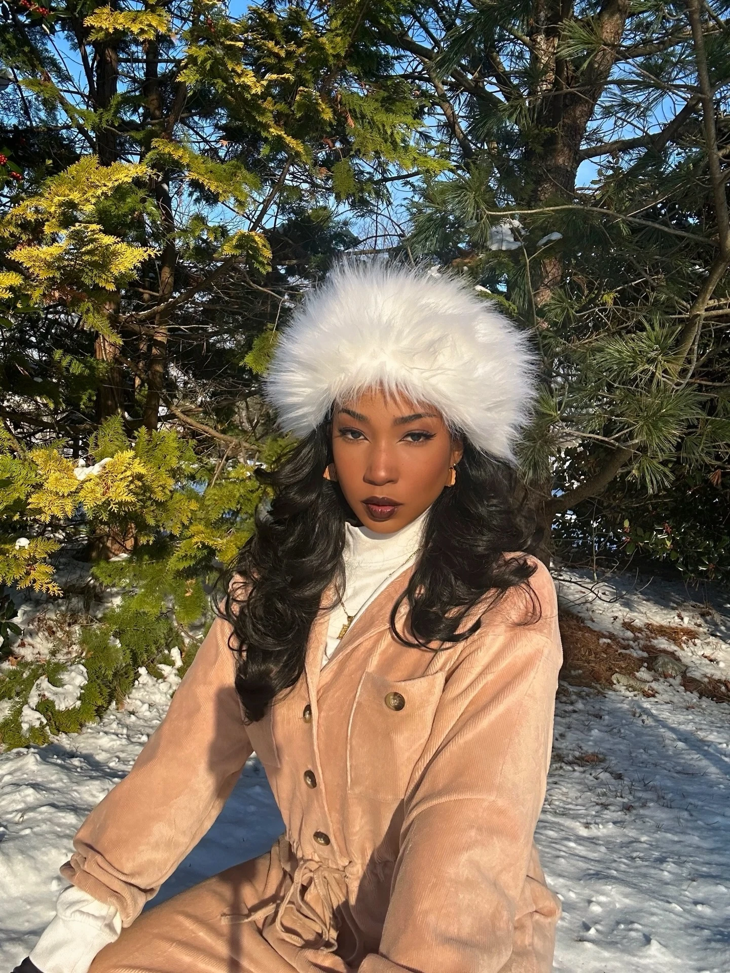 Person wearing a peach button-front jumpsuit over a white high-neck layer with a large fluffy white hat.