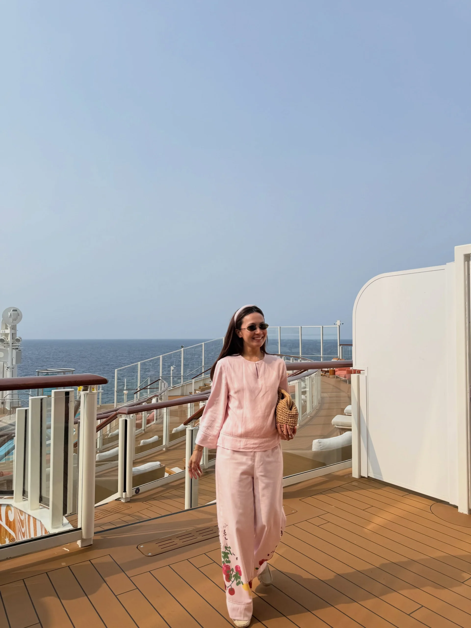 Woman in a pink linen top, floral embroidered wide-leg pants, and a woven straw bag.