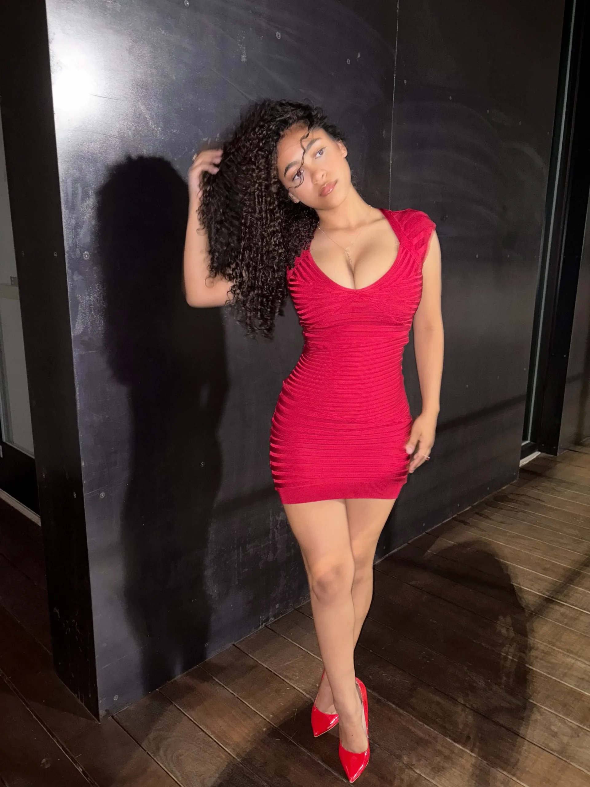 Woman in a bright red form-fitting bandage mini dress and matching red pointed heels.