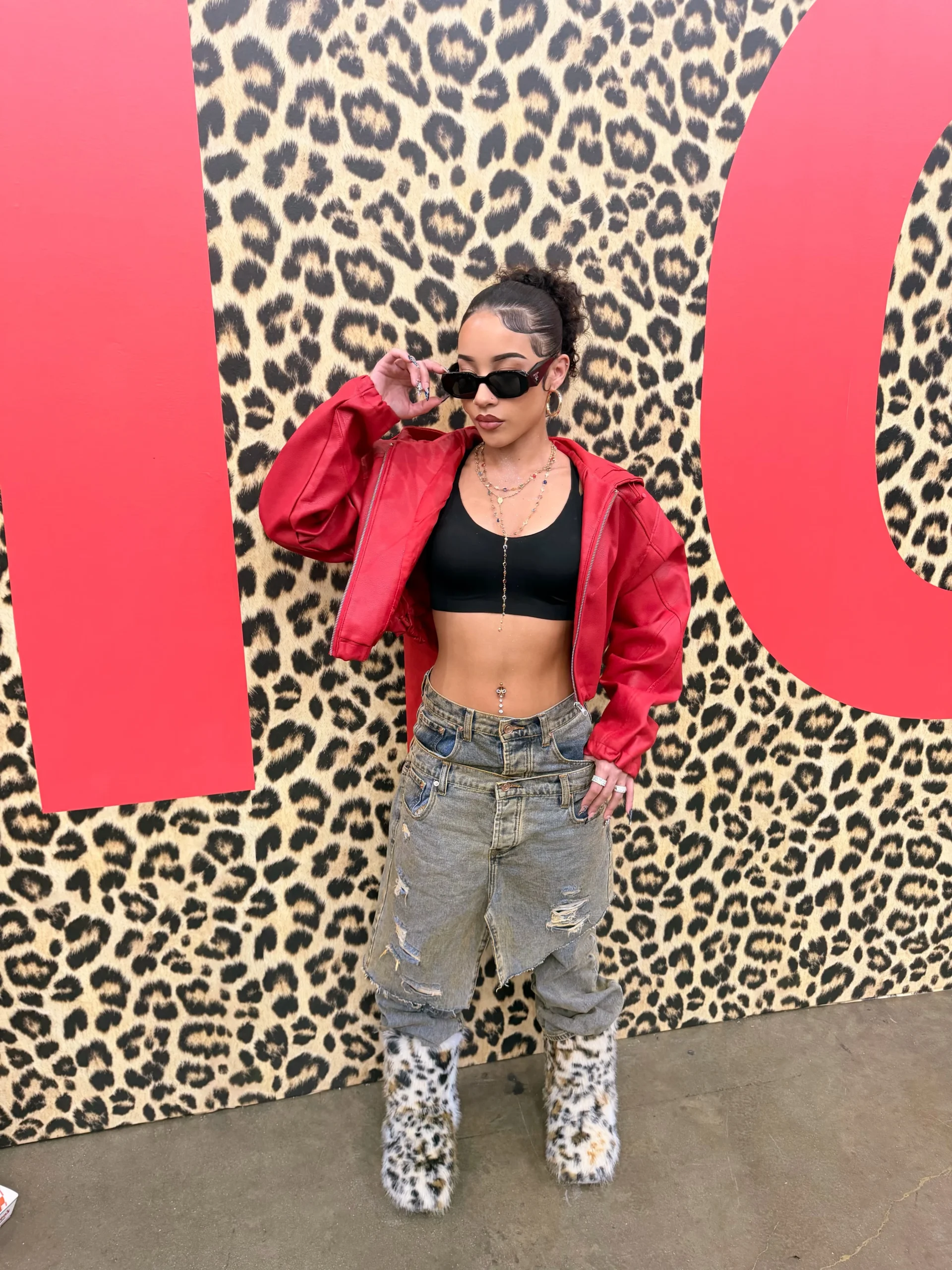Bright red cropped leather jacket over a black sports bra top with low-rise ripped light-wash jeans.