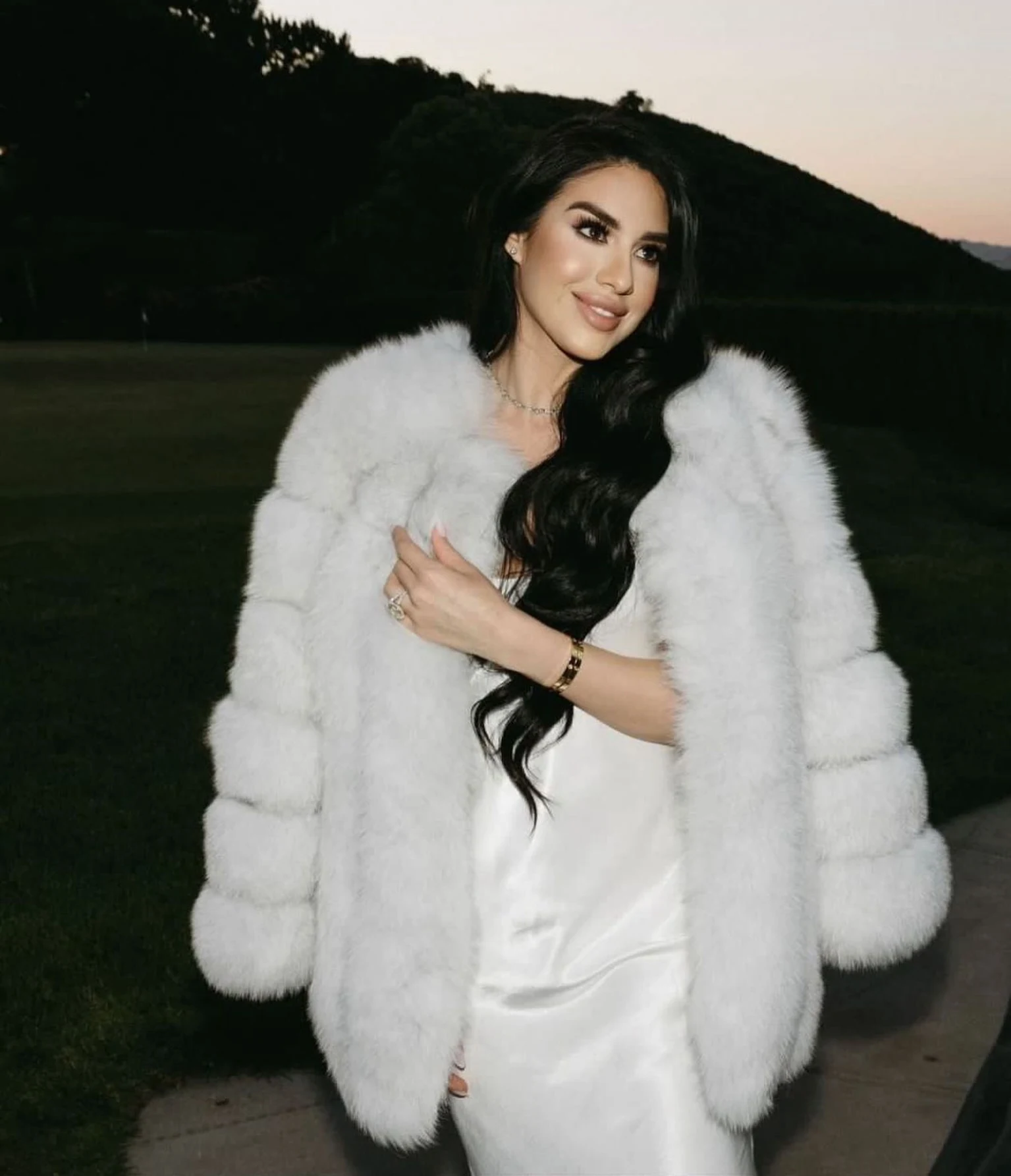 White slip dress layered beneath a voluminous white plush jacket worn open at the front.