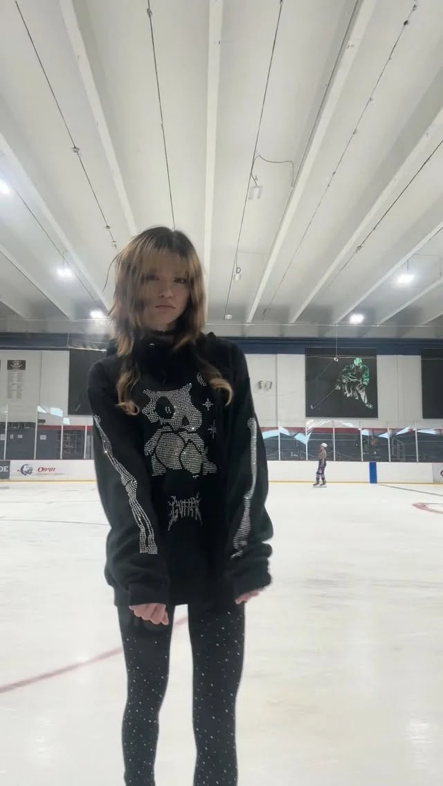 Person on an indoor ice rink wearing a black graphic sweatshirt and star-patterned black leggings.