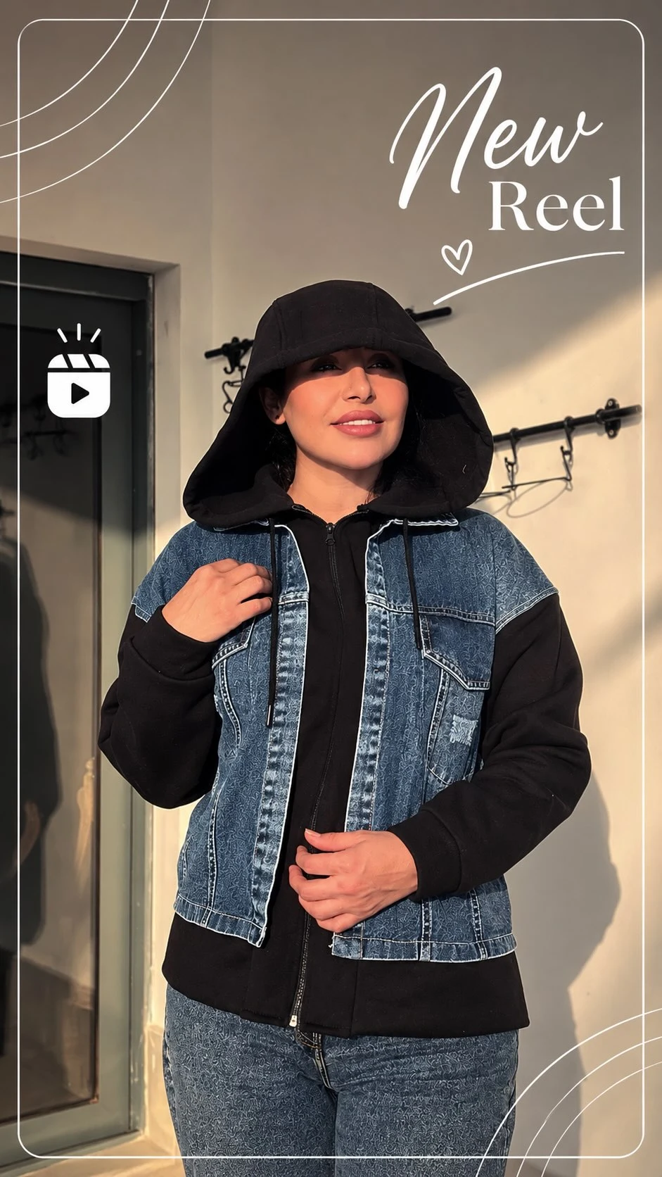 Person layering a black hooded sweatshirt under a blue denim vest with matching blue jeans.