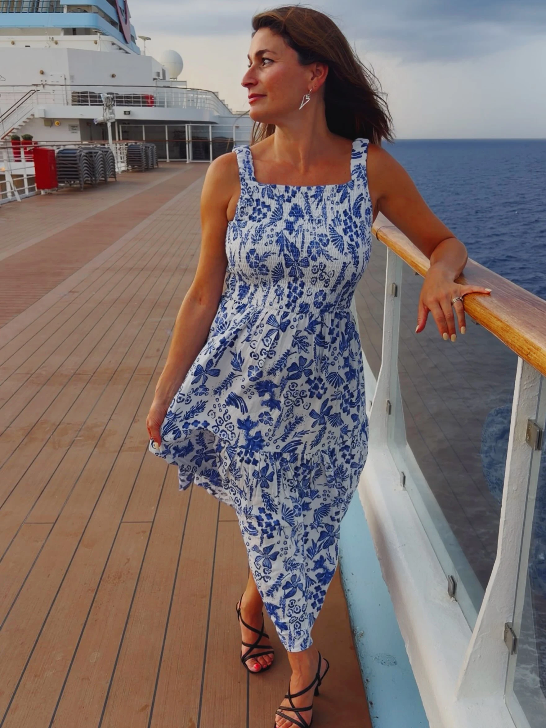 Woman wearing a sleeveless blue-and-white floral midi dress with black strappy high-heeled sandals.