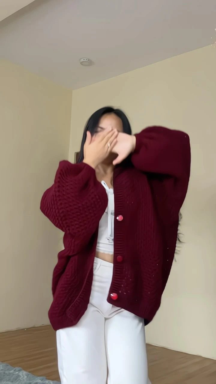 Oversized burgundy crochet cardigan with red buttons worn over a white crop top and loose trousers.