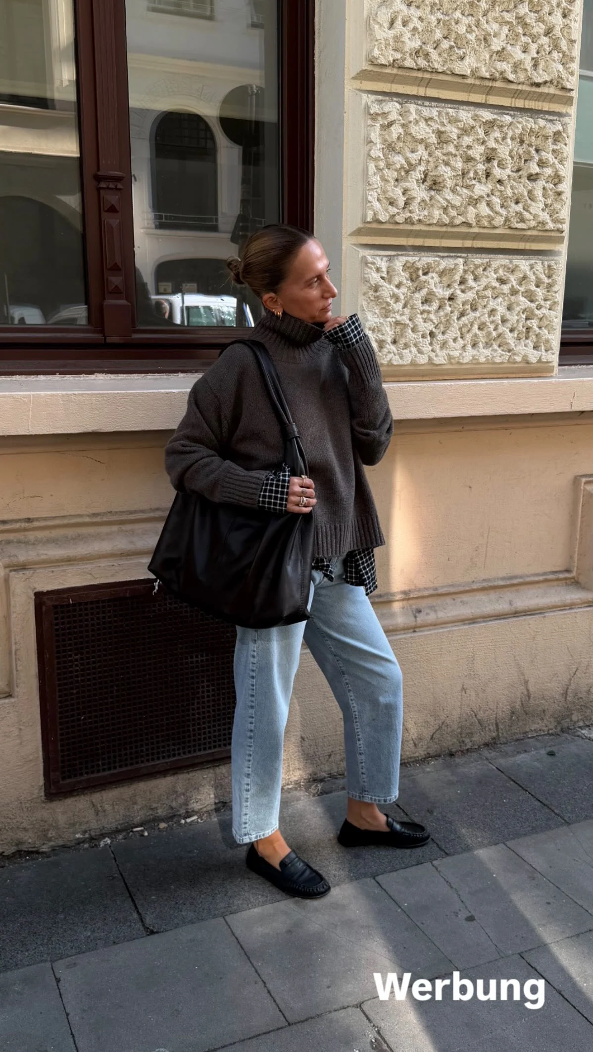 Person in charcoal turtleneck and cropped light blue jeans with black shoes and shoulder bag.