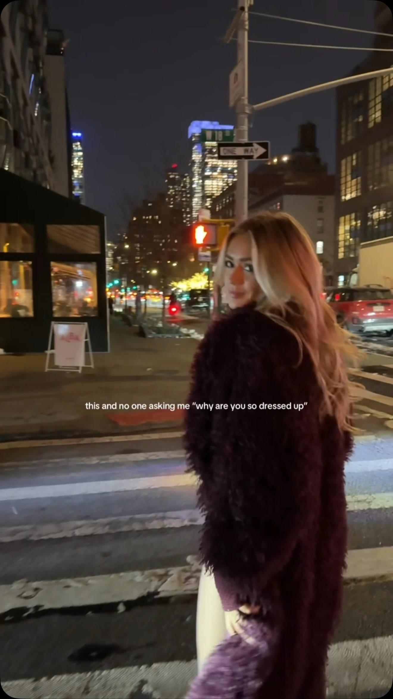 Woman wearing a long dark purple faux-fur coat over a sparkly burgundy mini dress with black boots.