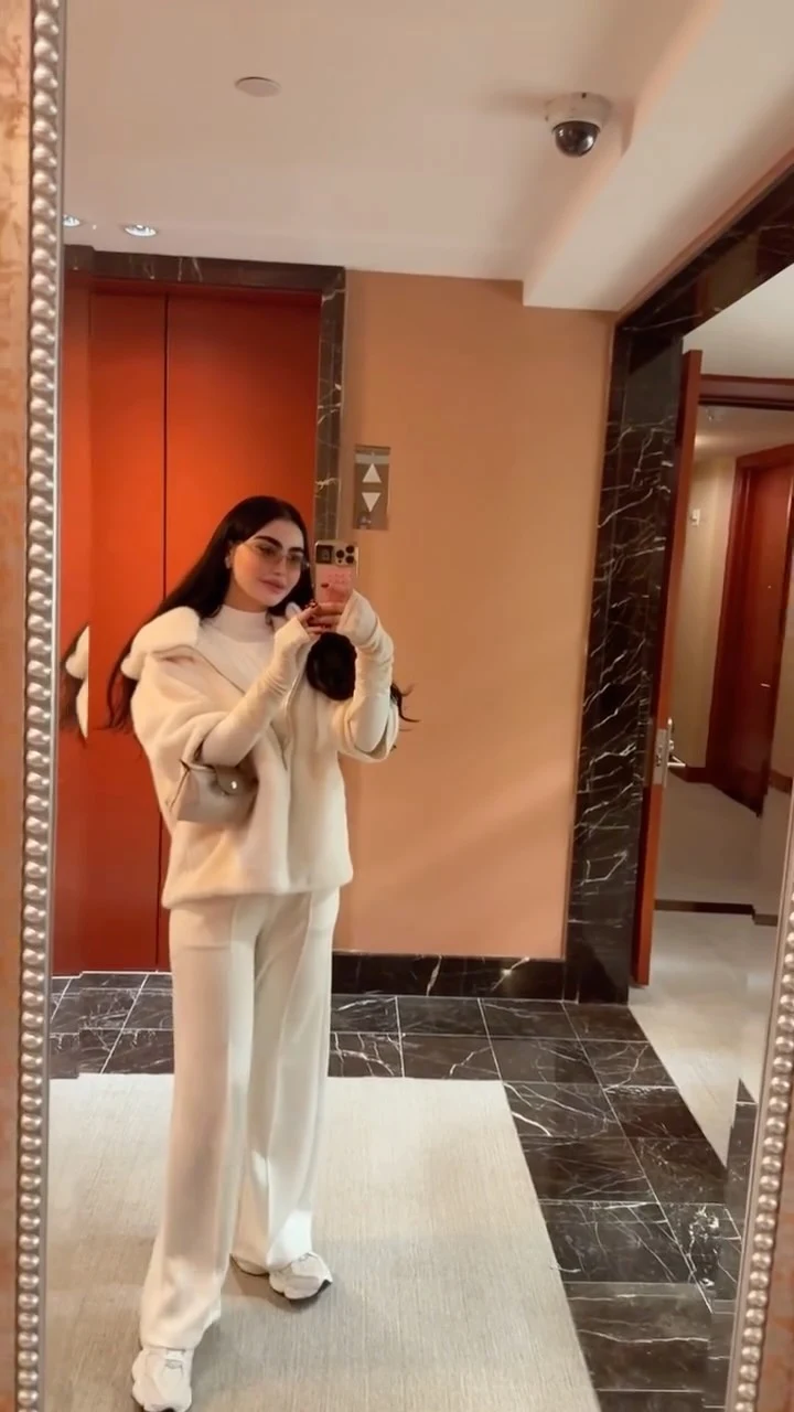 Woman in a fluffy cream hooded jacket, wide-leg trousers, and white shoes carrying a light shoulder bag.