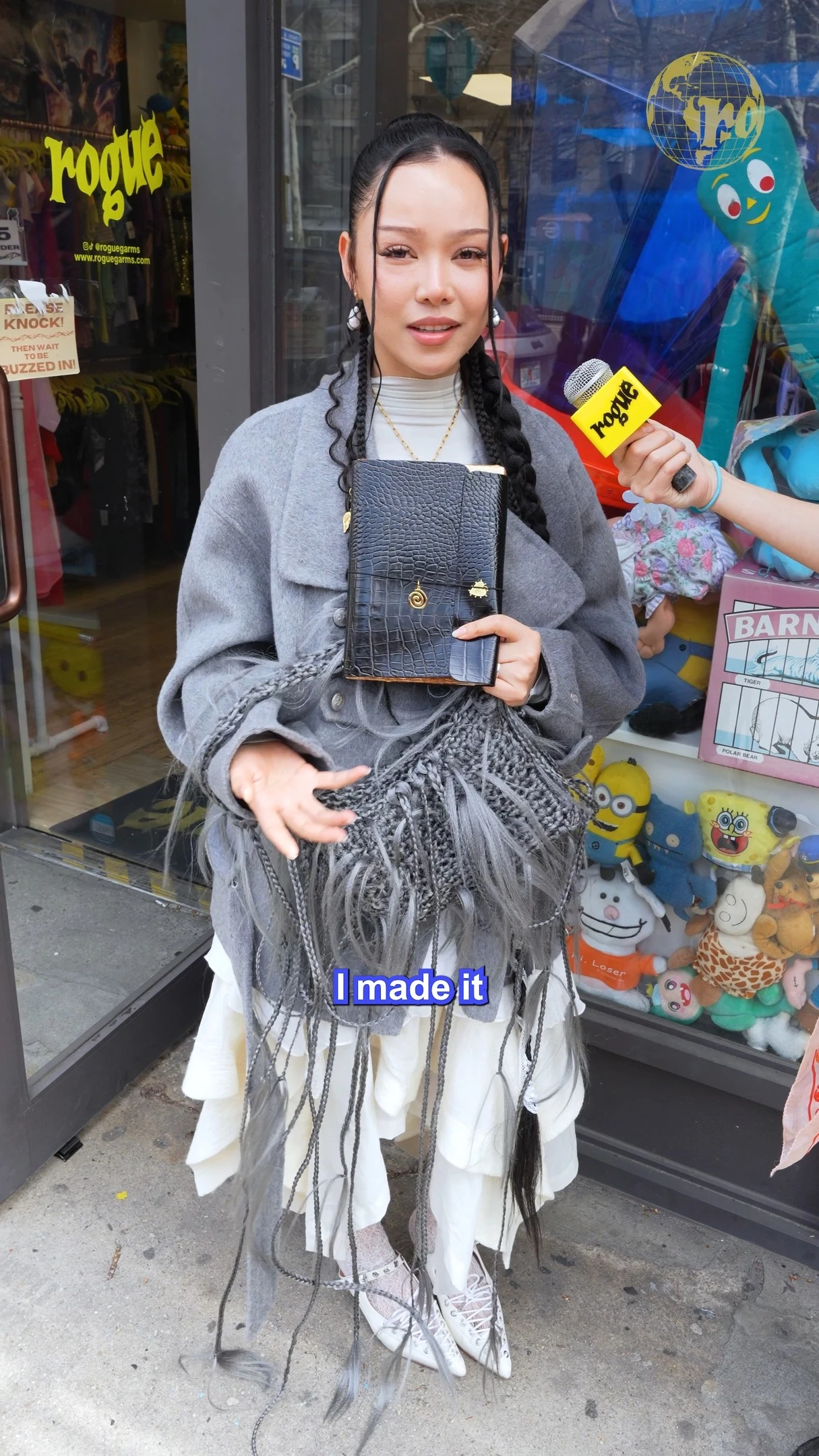 Gray wrap coat with fringed textile draped over a layered white skirt and white lace-up shoes.