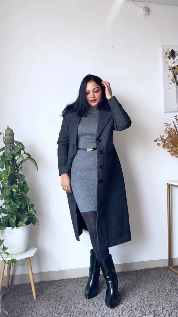 Woman in a grey wrap coat, cream ribbed knit dress, black tights, and heeled ankle boots.