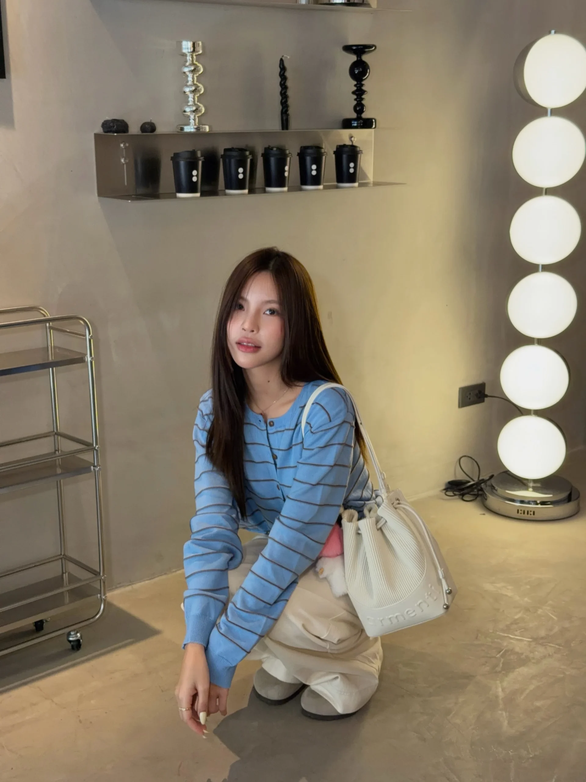 Light blue long-sleeve striped cardigan, cream wide-leg trousers, grey slip-on shoes and white ribbed drawstring bucket bag