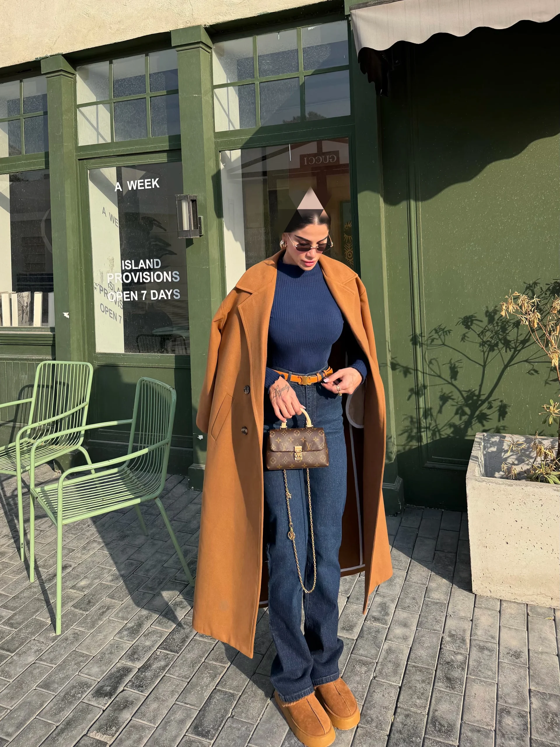 Long camel coat over navy ribbed top, blue jeans, platform shoes, and a handbag.