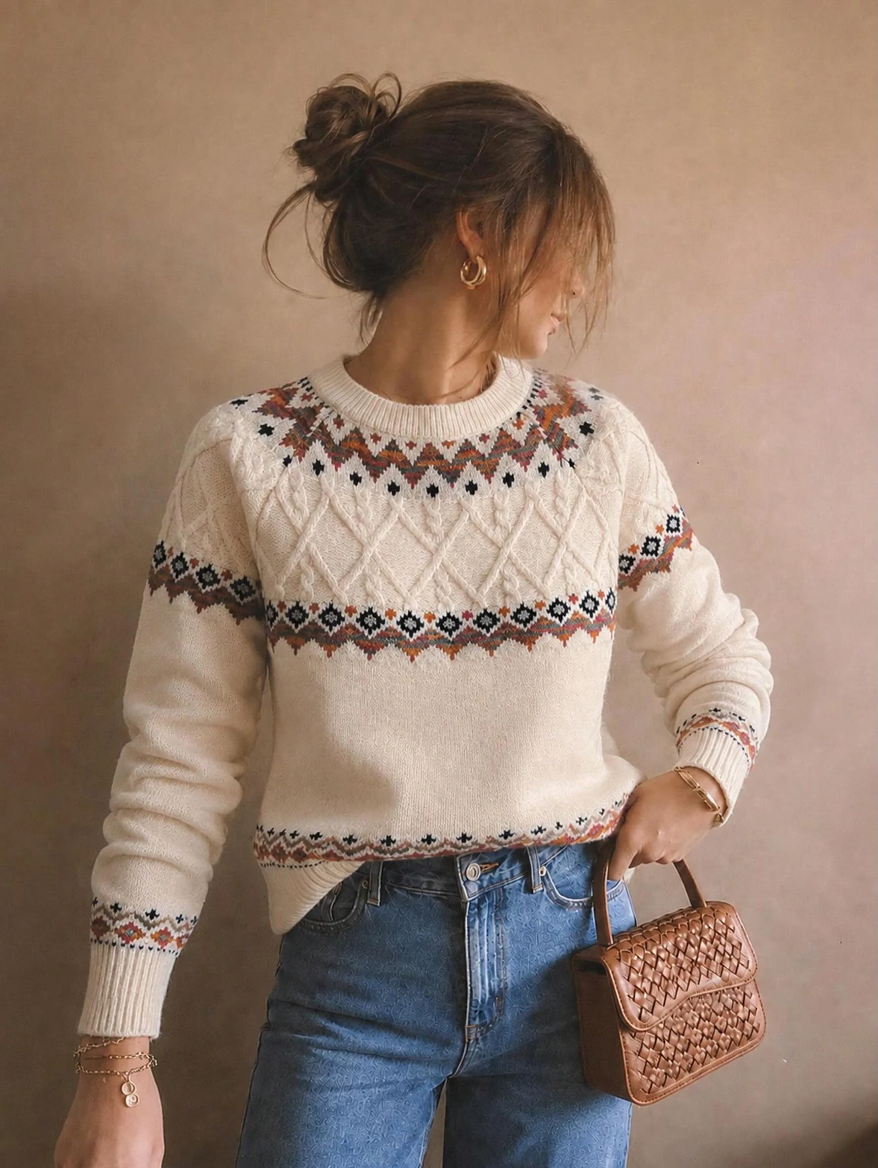 Cream Nordic pattern cable-knit sweater with high-waisted blue jeans and a small brown woven handbag.