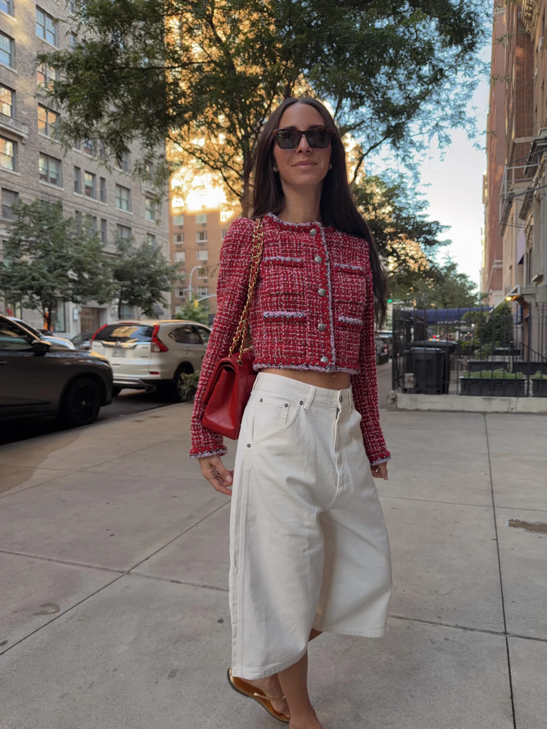 Red and white textured cropped jacket with white wide-leg pants, red chain-strap bag, and dark sunglasses.
