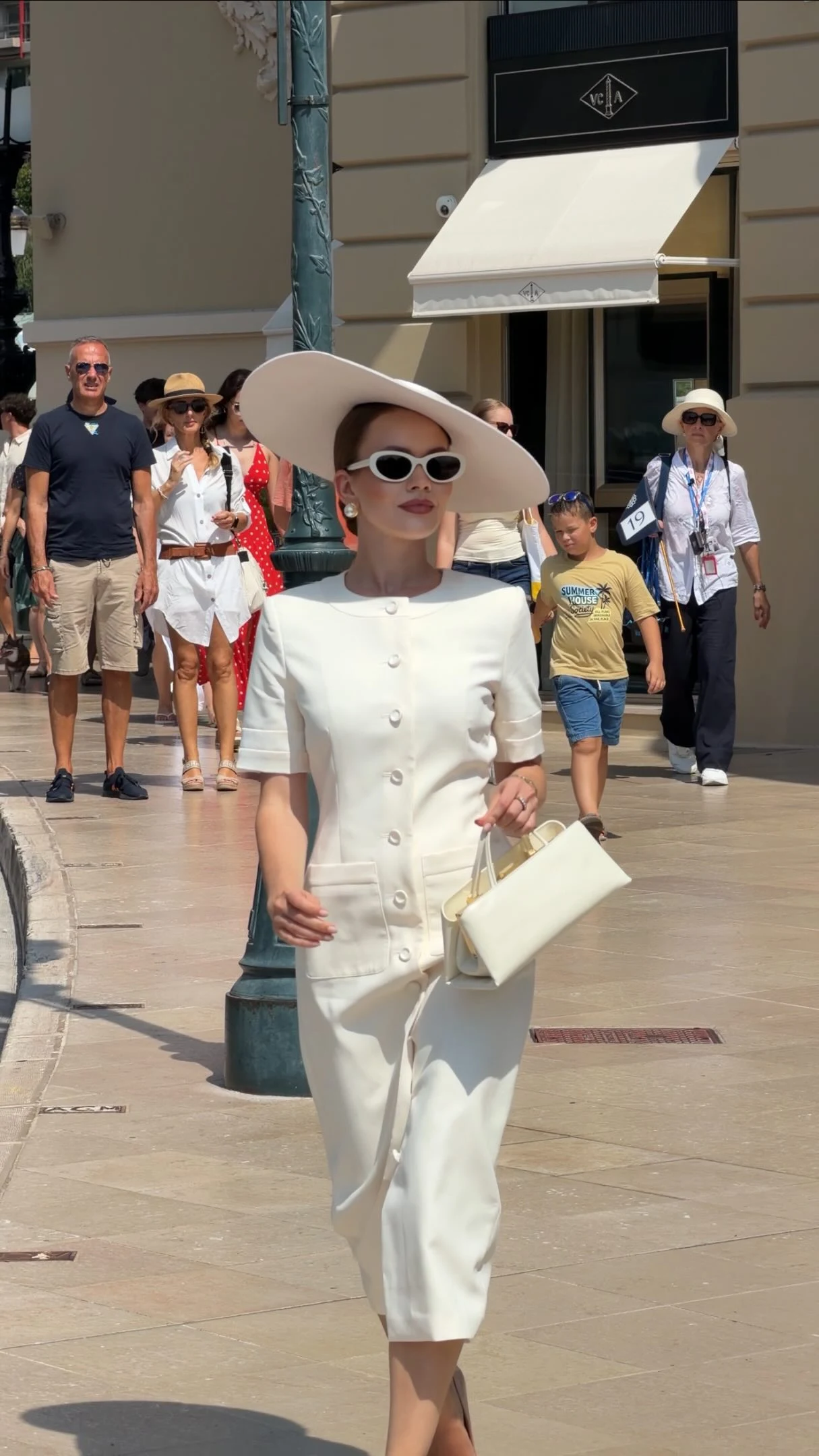 Monochrome white outfit with button-front top, cropped trousers, wide-brim hat, and oval sunglasses.