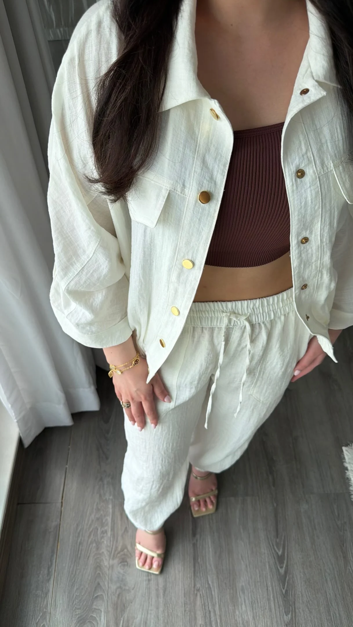 Person wearing an open white button shirt over a brown crop top with matching white pants.