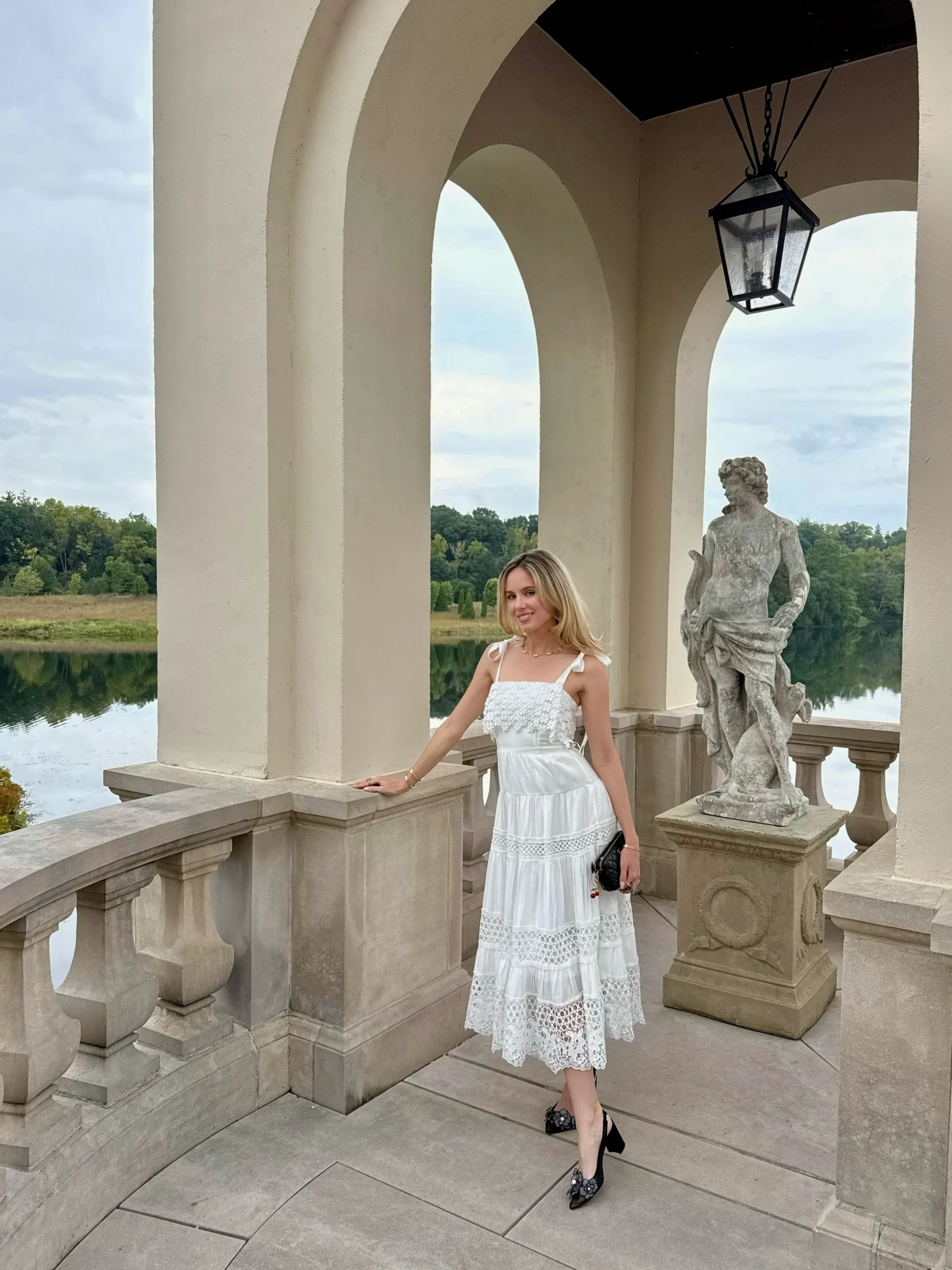 White sleeveless tiered lace midi dress paired with classic black heeled shoes.