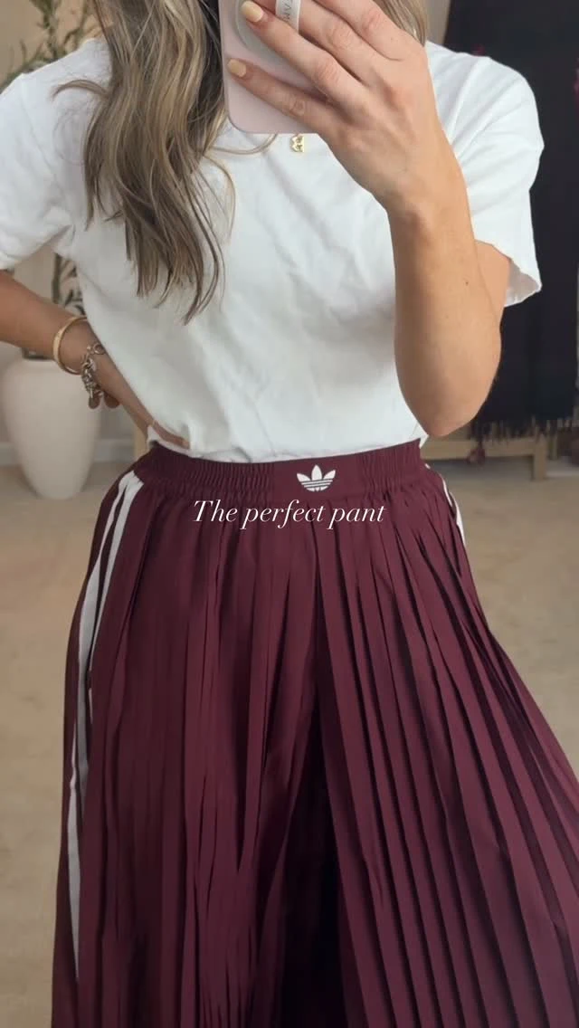 White T-shirt tucked into a high-waisted burgundy pleated skirt with gold pendant necklace and bracelets.