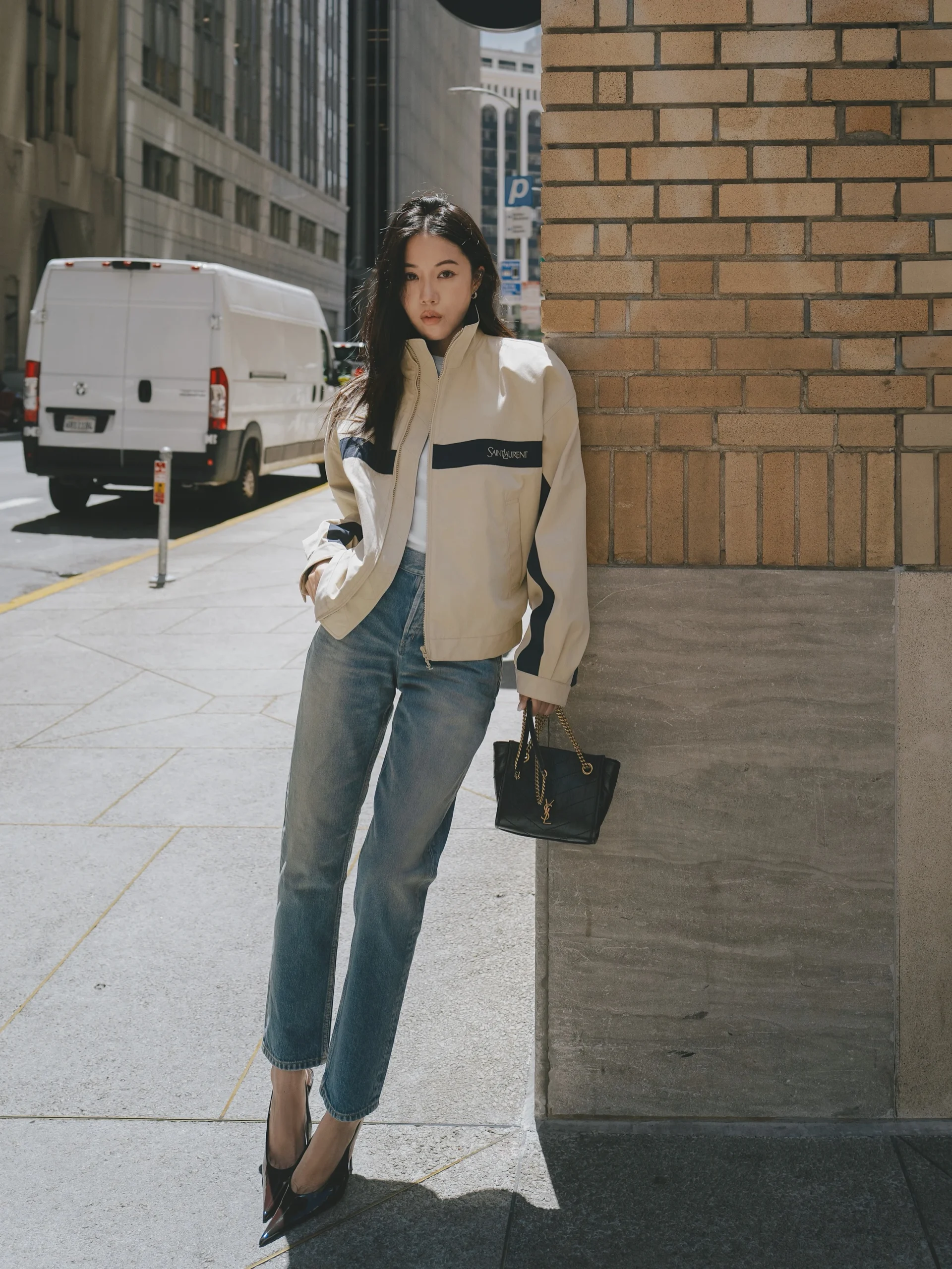 Beige jacket, blue straight-leg jeans, dark pointed heels, and structured black handbag styled together.