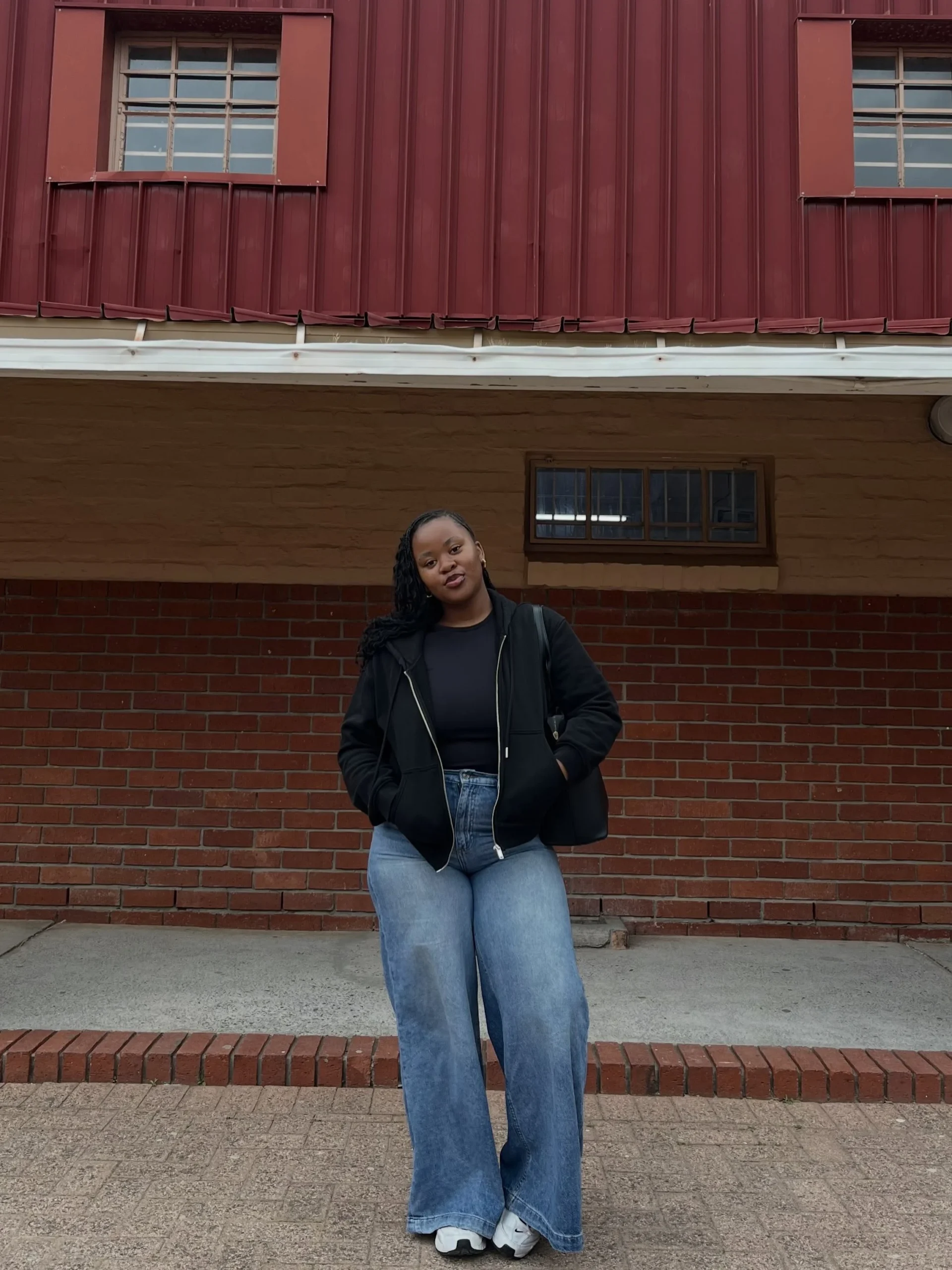Person in a black zip hooded jacket, light blue wide-leg jeans, and white sneakers.