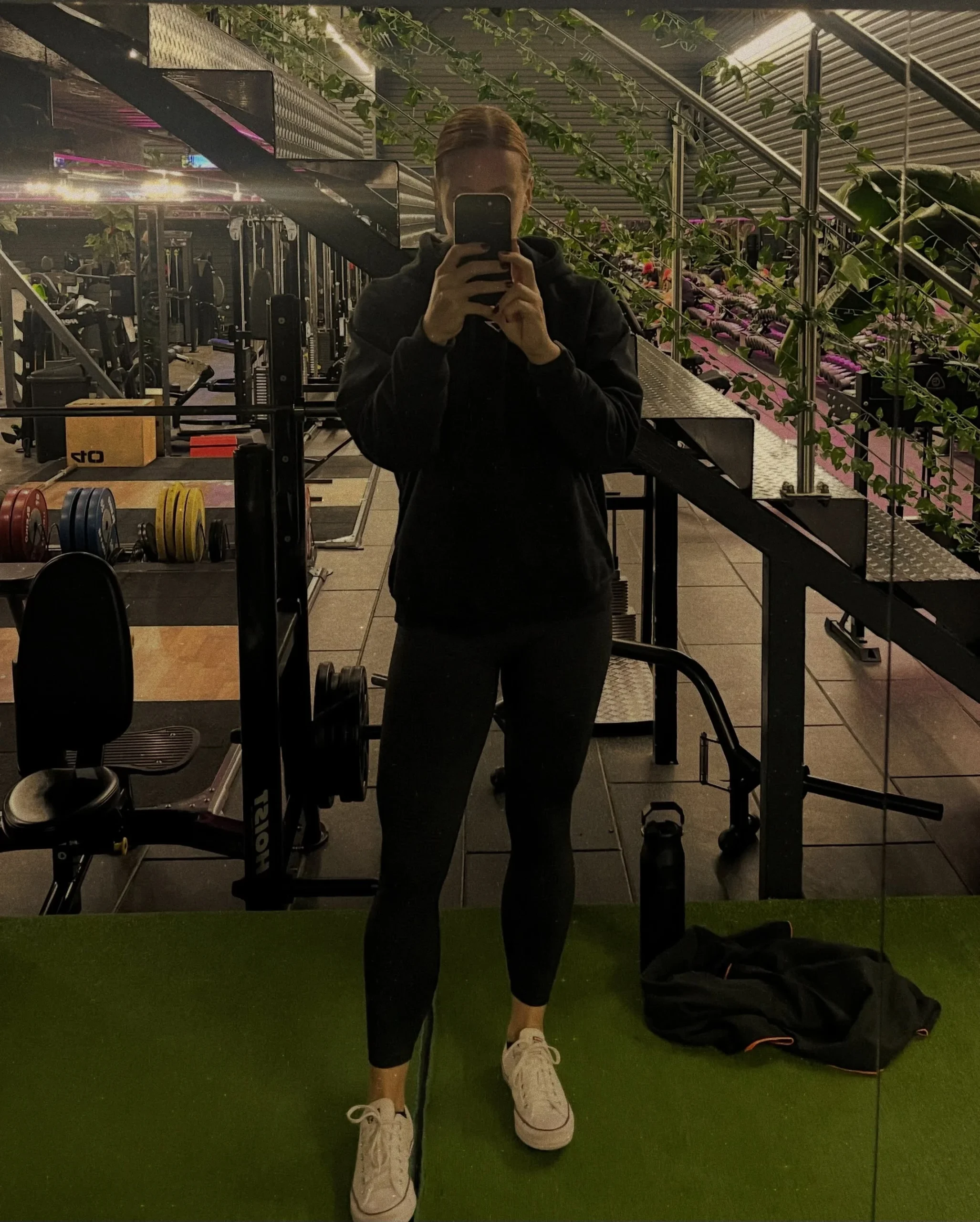 Black hoodie and fitted ankle leggings with white sneakers, gym mirror in background.