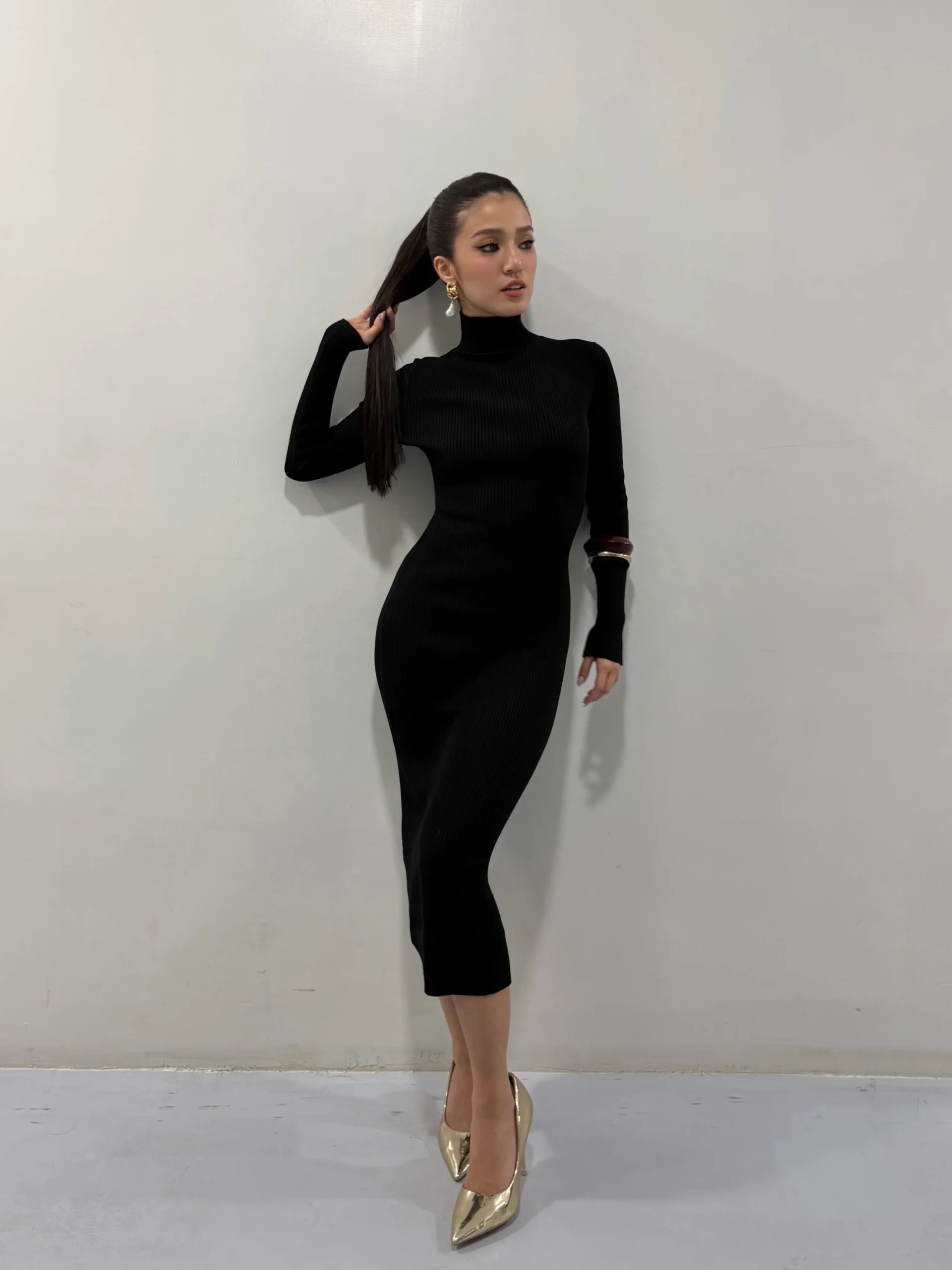 Fitted black ribbed midi dress styled with pointed gold heels and gold drop earrings.
