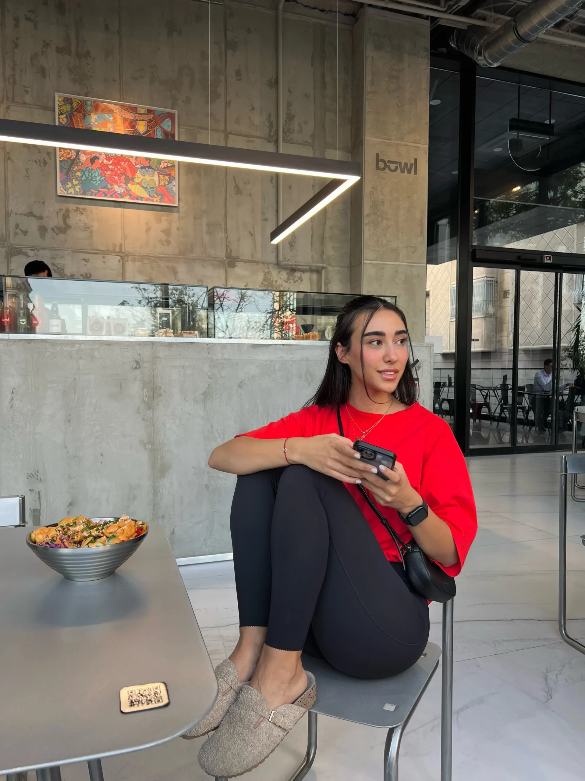 Bright red oversized tee styled with black leggings, beige slip-on shoes, and a small black crossbody bag.