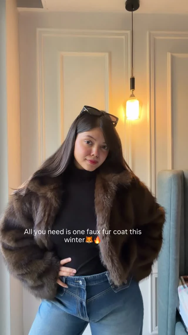 Woman in a brown cropped faux-fur coat, black turtleneck, high-waisted blue jeans, and sunglasses on her head.