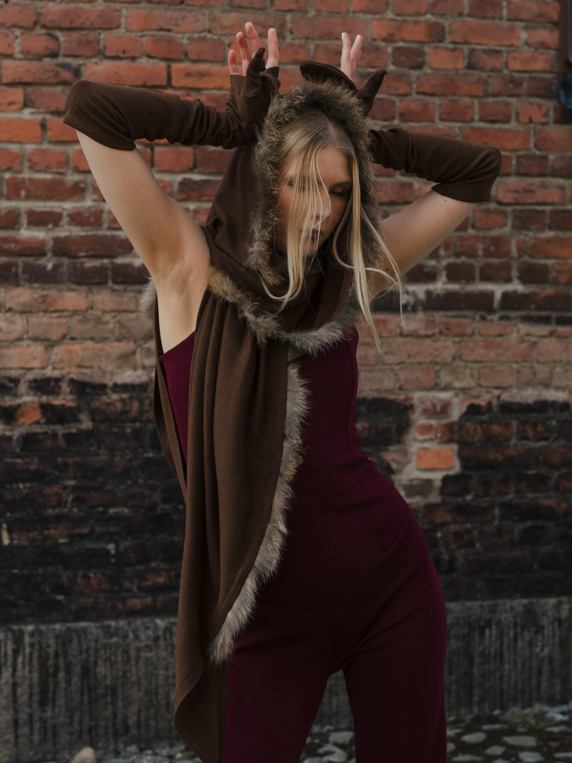 Person in a fitted burgundy jumpsuit with a long brown hooded fur-trim wrap draped over the shoulders.